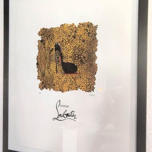 May include: Framed art print featuring a black high-heeled shoe silhouette on a leopard print background. The print includes the designer's signature in cursive script. The artwork is encased in a black frame.