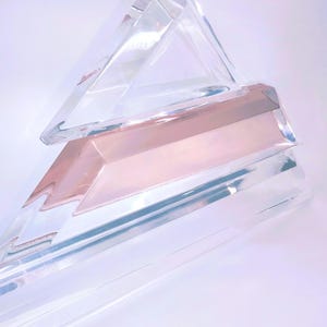 May include: A clear acrylic geometric sculpture with a pink, translucent, rectangular prism in the center.