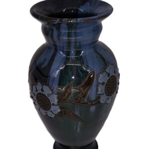 May include: A blue and green ceramic vase with brown floral accents. The vase has a wide mouth and a narrow base.