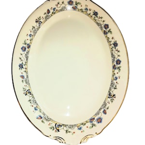May include: Oval serving platter with a cream-colored surface and a floral border. The border features blue, orange, and gray flowers with gold trim. The platter has a scalloped edge and is ideal for serving food.