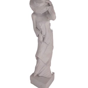 May include: White ceramic sculpture of a woman wearing a hat and a long dress. The sculpture is standing on a square base.
