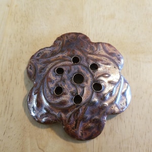 May include: A brown and purple ceramic flower-shaped dish with six holes. The dish has a swirl pattern.