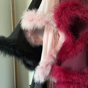 Puede incluir: Tres batas con ribete de plumas. Una es negra, otra rosa y otra burdeos.