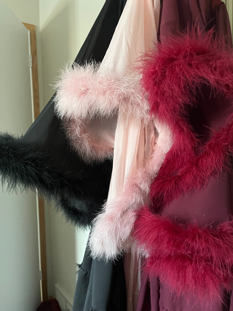 Puede incluir: Tres batas con ribete de plumas. Una es negra, otra rosa y otra burdeos.