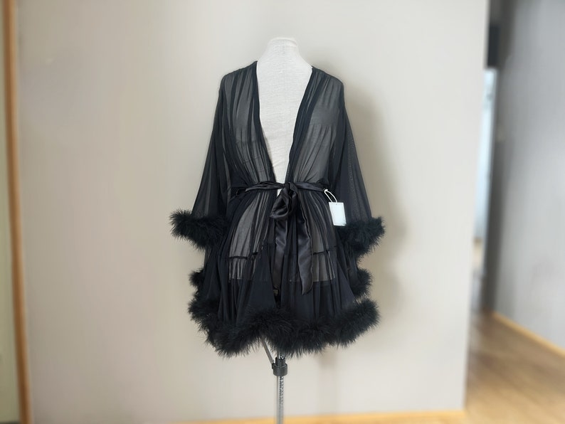 May include: A black sheer robe with a satin sash and feather trim. The robe is on a white mannequin.