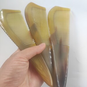 May include: Three horn combs with a natural, translucent appearance. The combs have a curved handle and fine teeth, ideal for hair care. The color varies from light to dark brown, with a polished finish.