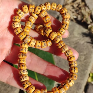 May include: A strand of light brown beads with etched cross and circle designs. The beads are strung together, forming a necklace or bracelet. The beads have a slightly aged appearance.