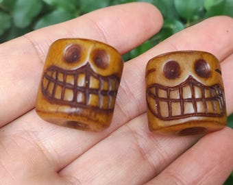May include: Two brown wooden beads with carved smiling faces. The beads have a hole in the center for stringing.