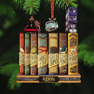 May include: A decorative Christmas ornament featuring seven Harry Potter book spines arranged in a row on a stone-textured base labeled KEVIN. Atop the books sit a red steam locomotive, a light blue flying car, and a purple triple-decker bus.