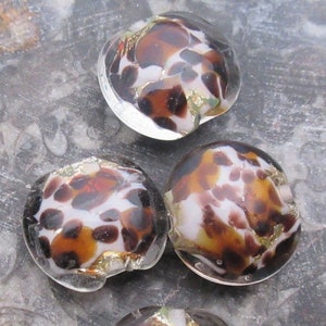 May include: Four round glass beads with a white background and brown and gold spots. The beads are translucent and have a glossy finish.