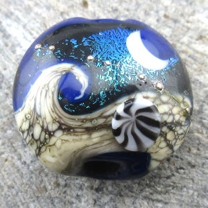 May include: A glass bead with a blue, black, white, and silver swirl design. The bead has a white and black swirl on one side.