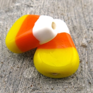 May include: Two candy corn shaped beads, one orange, white, and yellow, and the other yellow, orange, and white.
