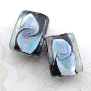 May include: Two square glass beads with a swirling pattern of white, blue, and black.
