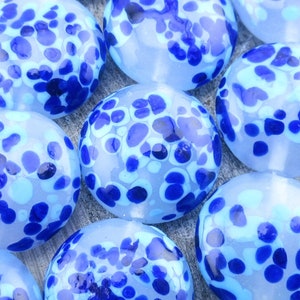 May include: A collection of blue and white glass marbles with a speckled pattern. The marbles are round and smooth, with a frosted finish.