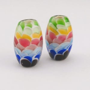 Puede incluir: Dos cuentas de vidrio ovaladas con un diseño colorido en capas. Las cuentas presentan un patrón de formas superpuestas en tonos de azul, rosa, amarillo, verde y marrón. Las cuentas son probablemente para la fabricación de joyas.