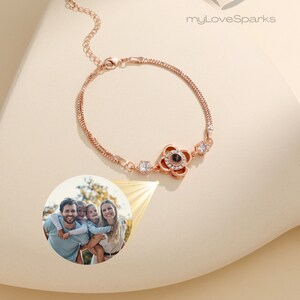 Puede incluir: Pulsera de oro rosa con un colgante en forma de flor que proyecta una foto. La pulsera tiene una cadena fina y está adornada con piedras redondas y transparentes. La imagen también incluye el texto "myLoveSparks".