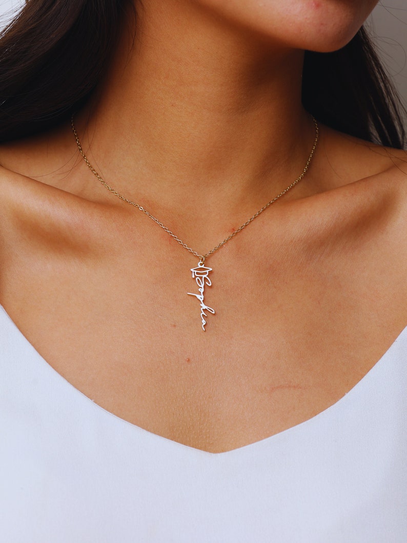 May include: A gold necklace with a graduation cap charm and the word "Sophia" written in cursive.