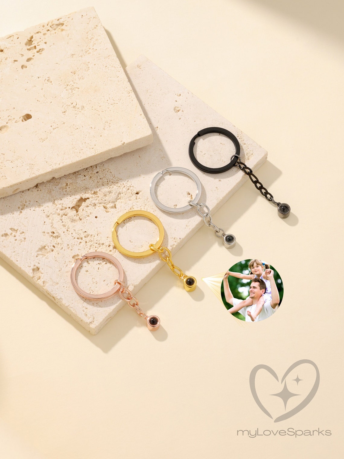 May include: Four keychains with a small round charm attached to a chain. The charms are black, silver, gold, and rose gold. The charms have a small black dot in the center. The keychains are displayed on a white textured surface. The image also includes a photo of a man and a child, and the text 'myLoveSparks'.
