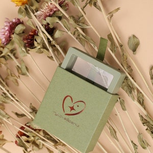 May include: A green box with the text "myLoveSparks" and a heart logo, holding a makeup palette. The palette has shades of pink, beige, and brown. The box is open, revealing the palette, and is surrounded by dried flowers.
