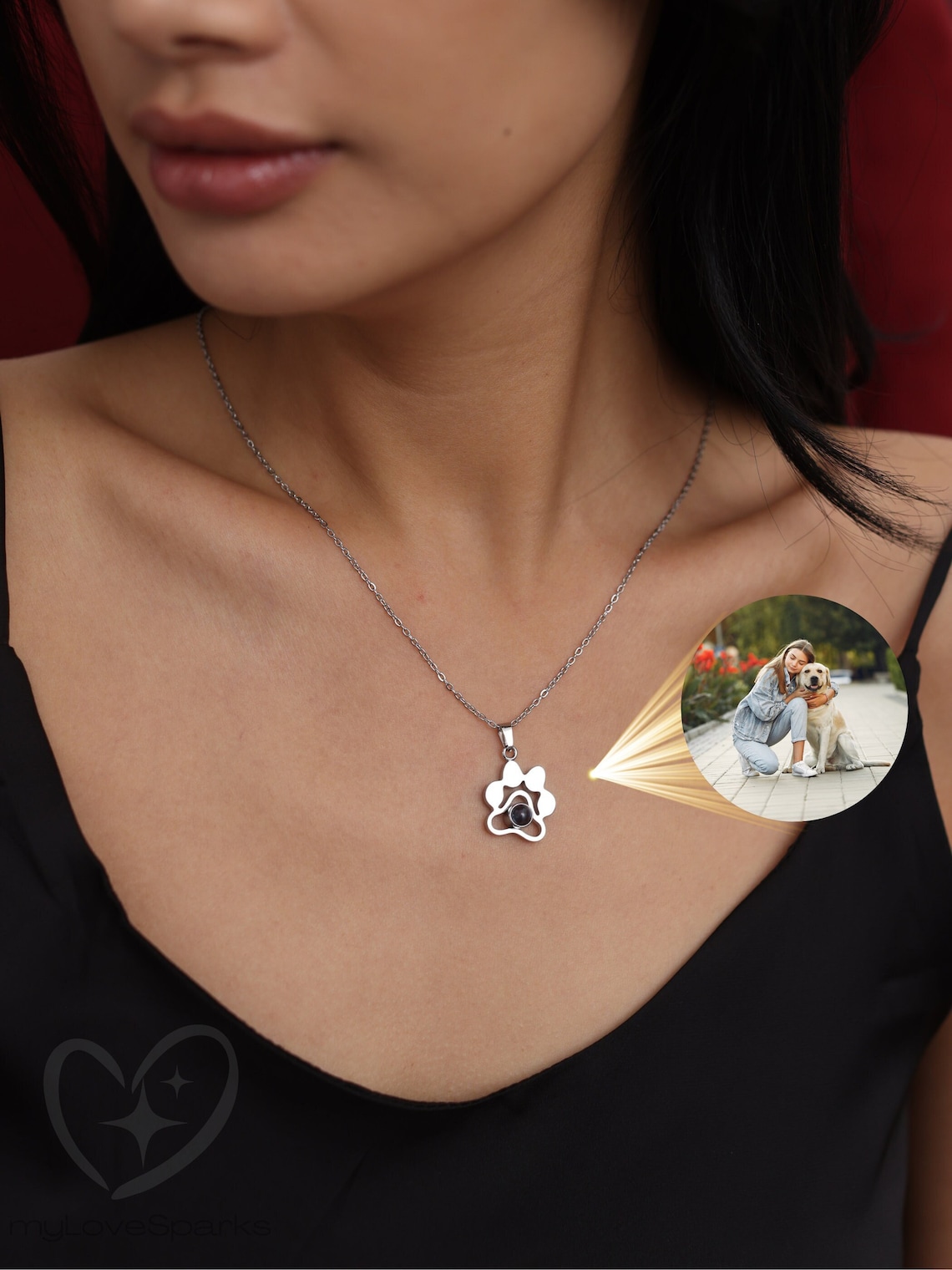 May include: A silver paw print necklace with a black photo inside. The photo is projected onto the surface below the necklace.