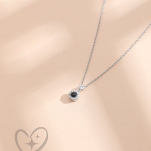 May include: A silver necklace featuring a small, round, black pendant surrounded by small clear stones. The delicate chain has a small, clear stone near the clasp. The logo "myLoveSparks" is at the bottom.