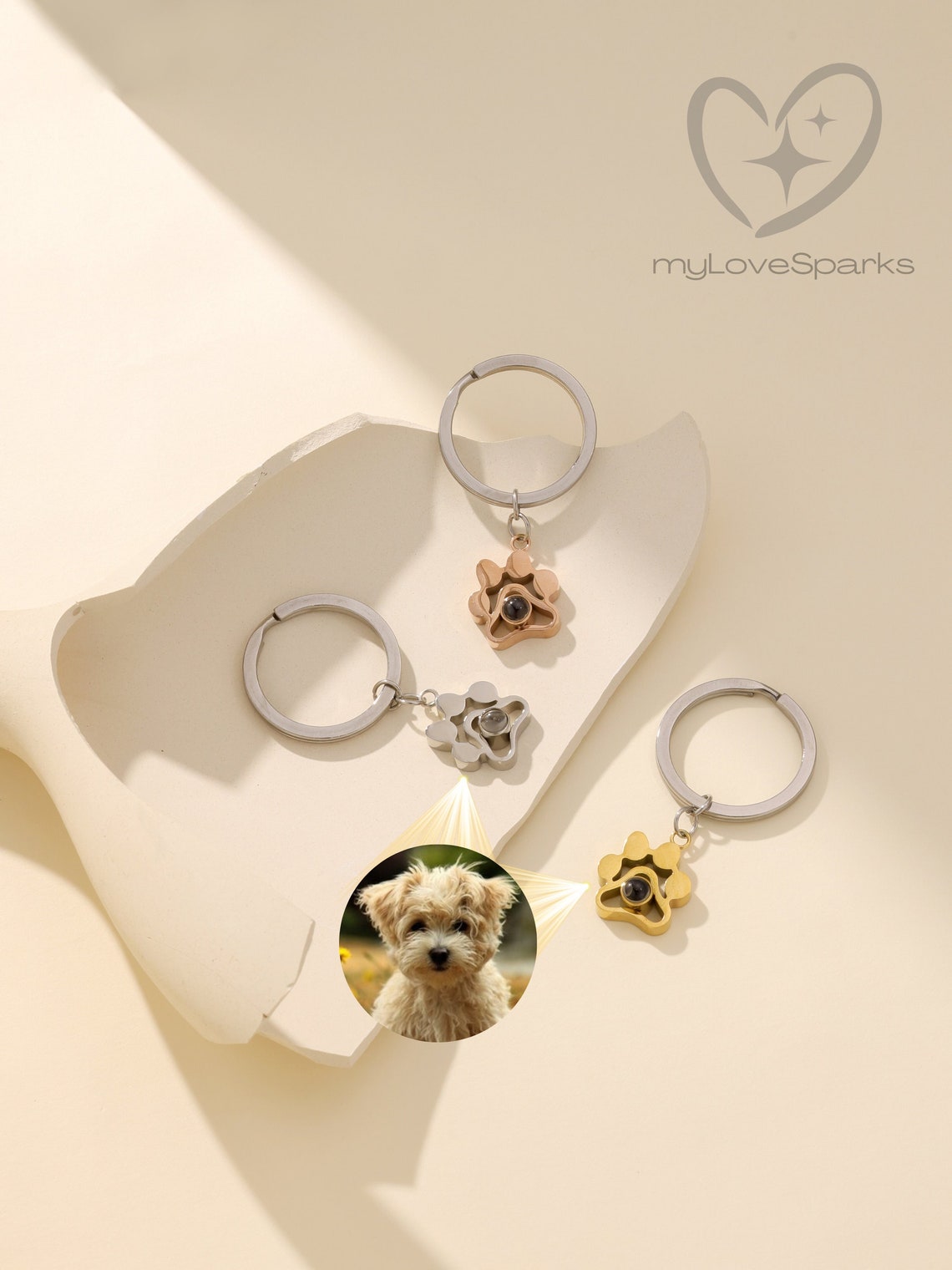 May include: Three silver keychains with a paw print charm. Each charm has a small, clear, round, glass-like insert that reflects a small image of a dog. The keychains are on a white surface. The text 'myLoveSparks' is in the upper right corner of the image.