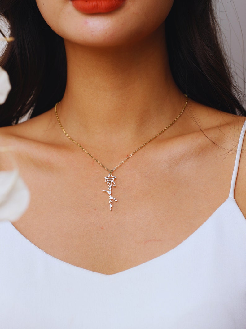 May include: A gold chain necklace with a pendant that says "Sophia" in cursive with a graduation cap above the name.