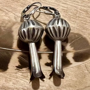 May include: A pair of silver earrings with a textured, round design. The earrings have a hook closure and a long, slender stem.