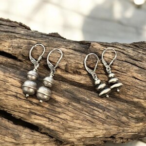 May include: A pair of silver dangle earrings with a layered design. The earrings have a hook closure and are made of metal.