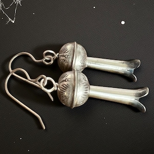 Peut inclure: Une paire de boucles d'oreilles argentées. Chaque boucle d'oreille présente un dessus arrondi et détaillé avec des motifs gravés et un bas long, fin et évasé. Les boucles d'oreilles ont des crochets incurvés pour oreilles percées.