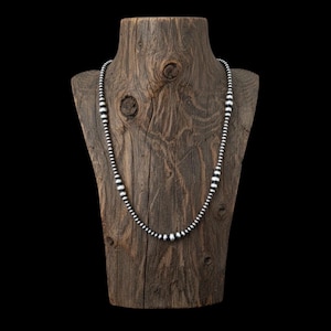 May include: A silver beaded necklace displayed on a rustic wooden jewelry bust. The necklace features a graduated design with larger beads in the center and smaller beads towards the ends. The wooden bust has a natural, weathered appearance.