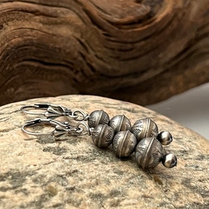 Puede incluir: Pendientes de plata con un racimo de cuatro cuentas redondas, cada una con un diseño texturizado. Los pendientes tienen un cierre de gancho.