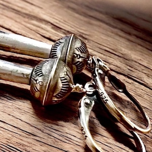 Puede incluir: Pendientes de plata con un diseño geométrico y un sello 925. Los pendientes cuelgan de una superficie de madera.