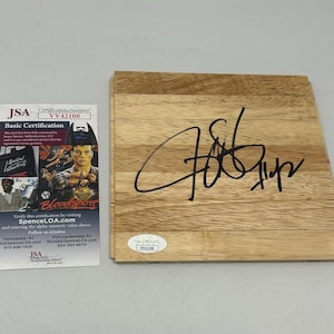 May include: A wooden plaque with a black signature on it. The plaque is light brown and has a grain pattern. The signature is of "Jeff Hornacek".