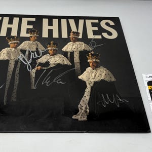 May include: A black vinyl record with the band name "THE HIVES" in white lettering. The album cover depicts five figures in crowns and capes, with signatures. A certification label is also visible.