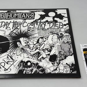 Może przedstawiać: Czarno-biała okładka albumu "The Day the Country Died" zespołu Subhumans. Grafika przedstawia postać punka, księdza i chaotyczną scenę. Zawiera kartę certyfikacji JSA Basic.