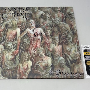 May include: A square vinyl record cover for Cannibal Corpse's The Bleeding, featuring a detailed illustration of numerous figures in muted tones. A black ink signature is centred on the cover. A JSA basic certification card is placed to the right.