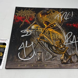 May include: A signed album cover featuring a skeletal figure with a scythe, a glowing planet, and an hourglass. The artwork is dark with red and gold accents. The album title "Death Atlas" is at the bottom.