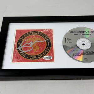 May include: Framed Queensrÿche "Rage for Order" CD and artwork. The artwork is red with a circular design and the text "Queensrÿche Rage for Order". The CD is silver with black text. Includes a JSA Basic Certification card.