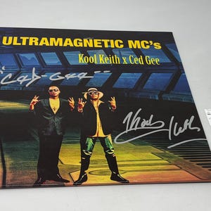 以下が含まれることがあります： Ultramagnetic MC'sのKool Keith x Ced Geeのサイン入りアルバムカバー。アルバムアートは、スーツとサングラスをかけた2人の男性を示しています。カバーは白いインクで署名されています。JSA Basic Certificationステッカーが見えます。