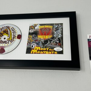 Pode incluir: Uma apresentação emoldurada com um CD assinado e um single de CD em forma de bolo de Chad Smith's Bombastic Meatbats. A capa do CD apresenta uma ilustração de desenho animado de uma banda tocando música. O single de CD em forma de bolo é decorado com o logotipo da banda e as palavras "Chad Smith's Bombastic Meatbats". A apresentação é autenticada pelos serviços de autenticação JSA.