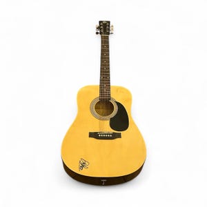 May include: Acoustic guitar with a natural wood finish. The guitar has a black pickguard, six tuning pegs, and a sound hole with a decorative rosette. The body has a signature on the lower bout. Suitable for musicians and music lovers.
