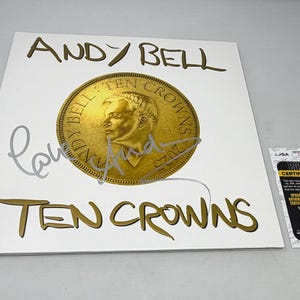 Może przedstawiać: Biała okładka albumu ze złotymi literami i złotym wzorem monety. Widoczny jest tekst "ANDY BELL" i "TEN CROWNS". Album jest podpisany srebrnym tuszem. Naklejka certyfikacyjna znajduje się po prawej stronie.