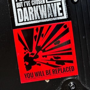 May include: A sticker with the text "BUT I'VE CHOSEN DARKWAVE" in white on a black background. Below, a red square features a black skull and radiating lines, with the words "YOU WILL BE REPLACED".