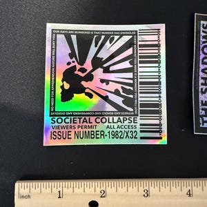 May include: Holographic sticker with a skull and abstract design. The sticker includes the text "Societal Collapse" and "Issue Number-1982/X32". The sticker is approximately 2 inches wide.
