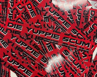 May include: A collection of red rectangular stickers with black and white text. The stickers feature the words "DIE YUPPIE SCUM" in a bold, sans-serif font. Additional text is visible at the bottom of the stickers.