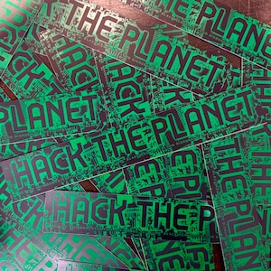May include: A collection of rectangular stickers with the words "HACK THE PLANET" in black, overlaid on a green circuit board design. The stickers have additional text in green and black.