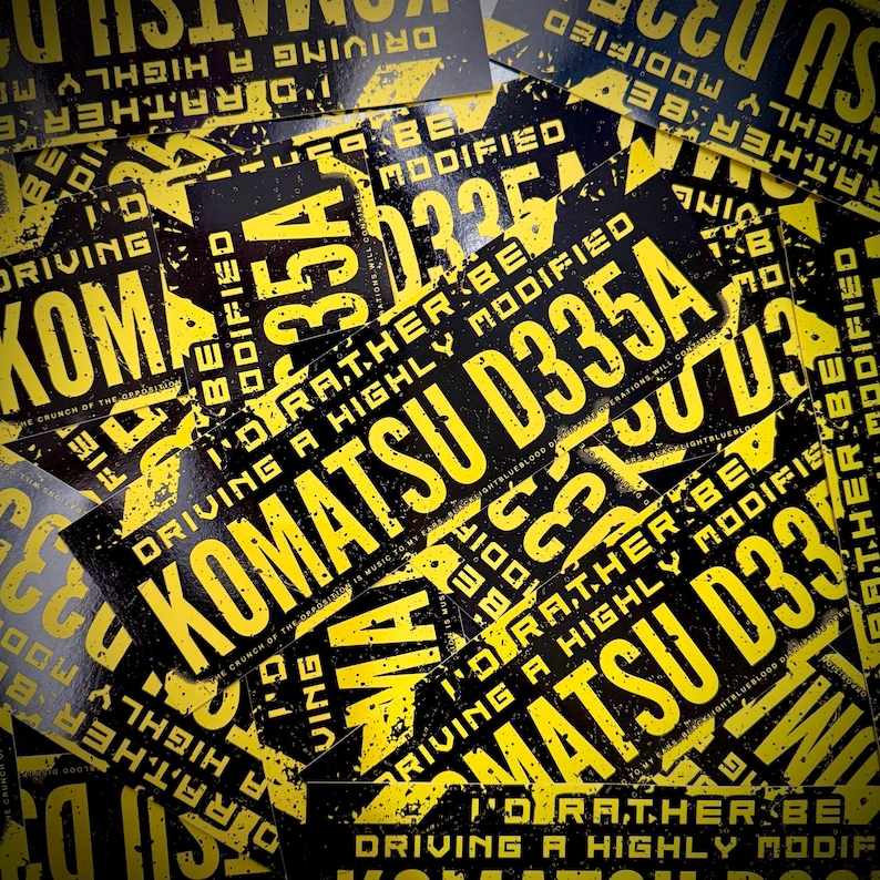 Puede incluir: Un conjunto de pegatinas negras y amarillas. Las pegatinas presentan el texto "KOMATSU D335A" y "I'd rather be driving a highly modified". El dise&ntilde;o tiene un aspecto desgastado.