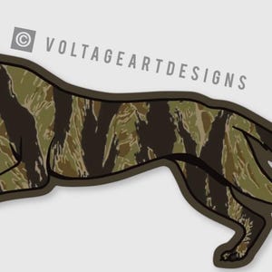 May include: A sticker featuring a running dog with a camouflage pattern in shades of green and brown. The dog has a black nose and ears, with its tongue sticking out. The text "VOLTAGEARTDESIGNS" is in the upper right corner.