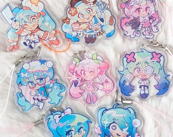 May include: A collection of eight clear acrylic charms featuring colorful anime-style characters with various expressions, outfits, and accessories. Each charm includes a metal jump ring and a thin cord for attachment, showcasing vibrant pastel color palettes.